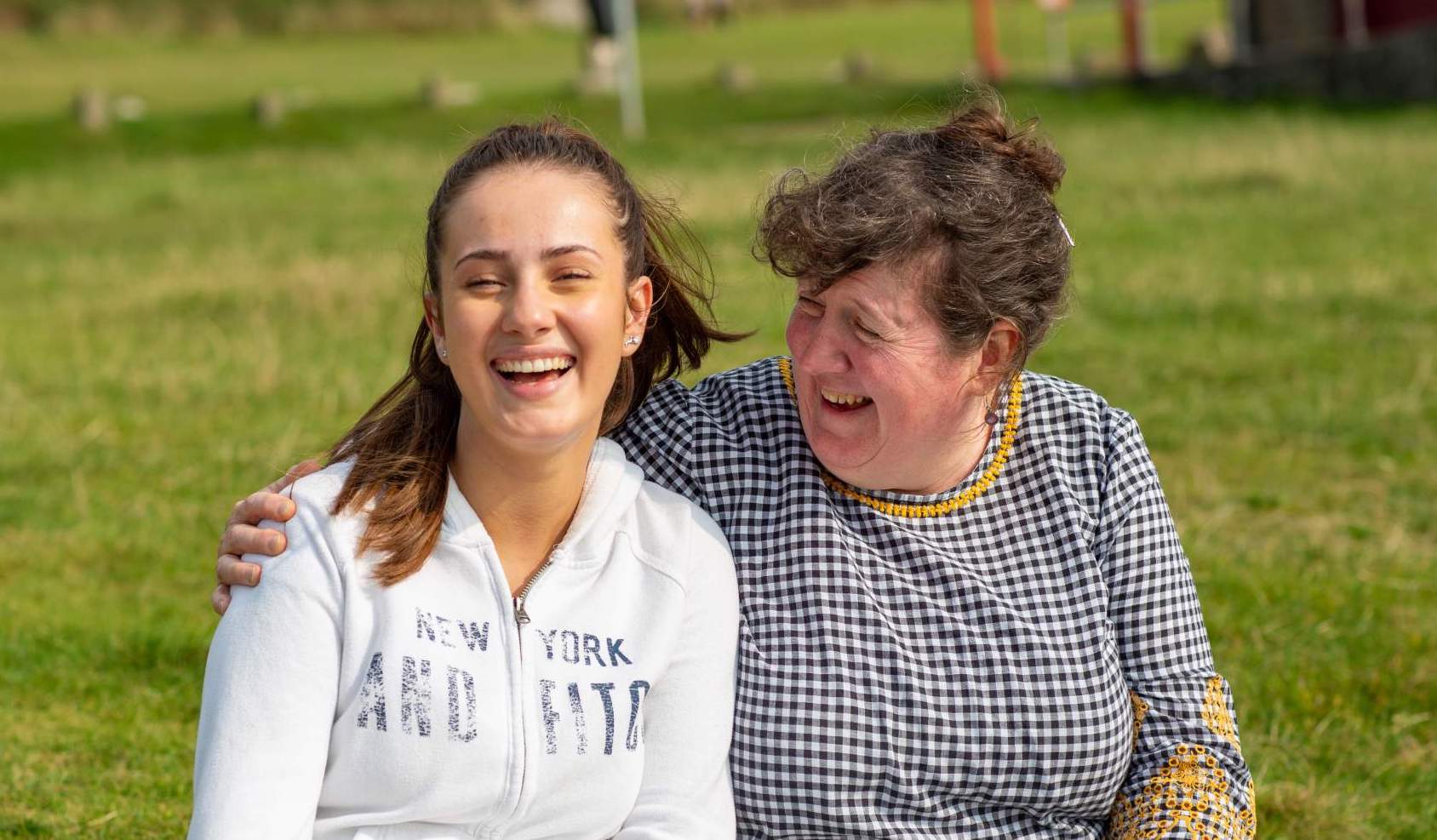 Mum and girl sitting on the grass laughing